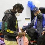 Taylor and a Seahawk assistant help students pick up coats at a school event.